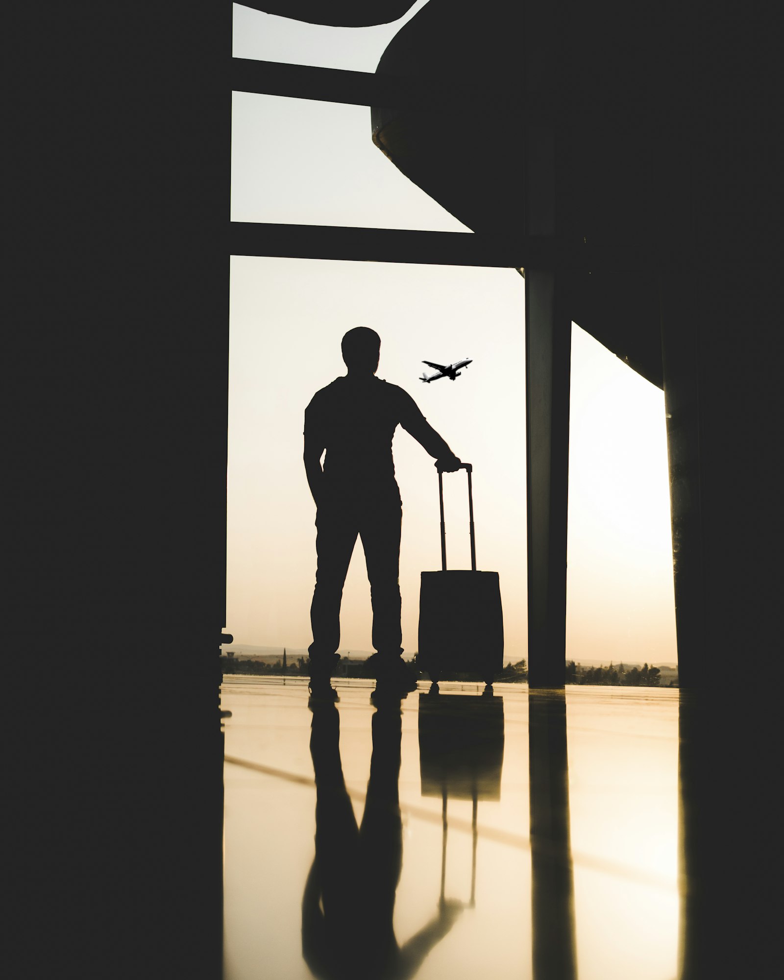 A traveler silhouetted against the sunset, watching a plane take off beside their luggage